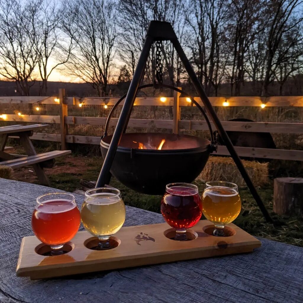 A flight of cider sitting on a wooden table in front of a fire in a hanging cauldron.