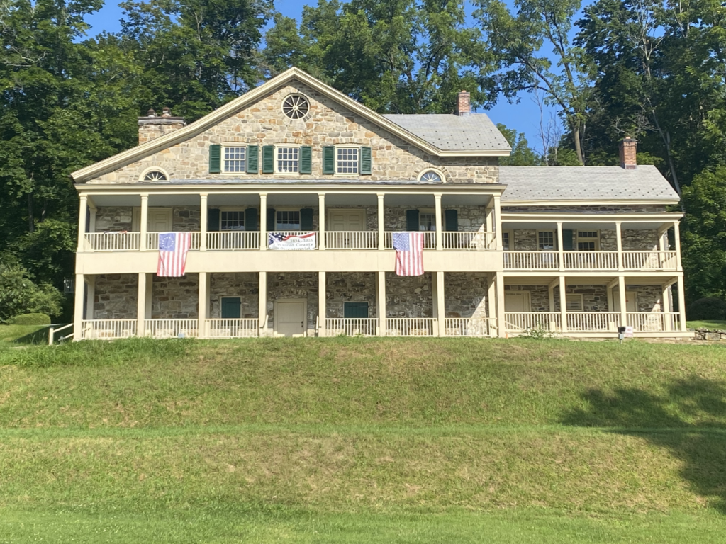 Light stone two story house with columns and balconies across the front and green shutters