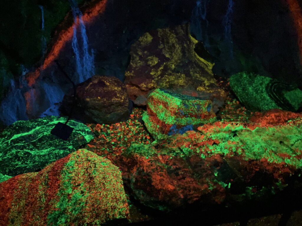 Minerals inside a mine glow in green, orange, and blue colors.